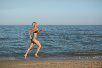 Image showing Side view of a woman running on the beach with the horizon and sea in the background