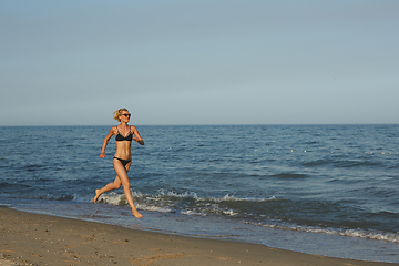 Image showing Side view of a woman running on the beach with the horizon and sea in the background