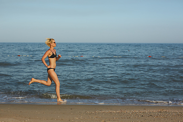 Image showing Side view of a woman running on the beach with the horizon and sea in the background
