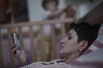 Image showing mother is using smarphone in bed while baby sleeping