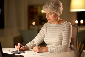 Image showing old woman counting on calculator at home at night