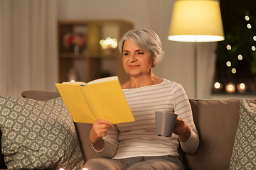 Image showing senior woman reading book and drinking tea at home