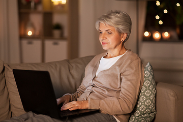 Image showing happy senior woman with laptop at home at night