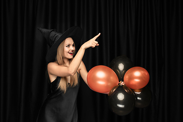 Image showing Young woman in hat as a witch on black background