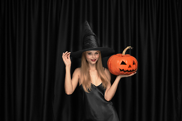 Image showing Young woman in hat as a witch on black background