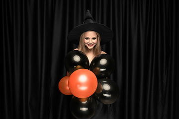 Image showing Young woman in hat as a witch on black background