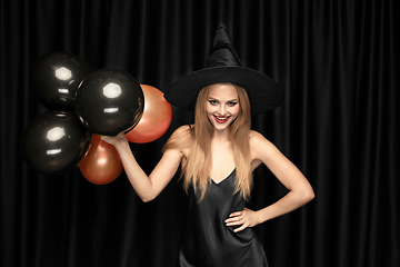 Image showing Young woman in hat as a witch on black background