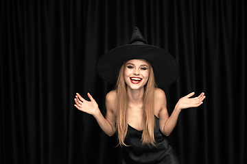 Image showing Young woman in hat as a witch on black background