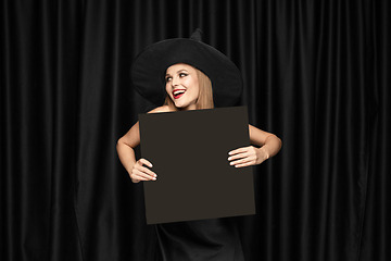 Image showing Young woman in hat as a witch on black background