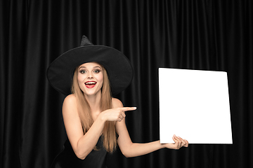 Image showing Young woman in hat as a witch on black background