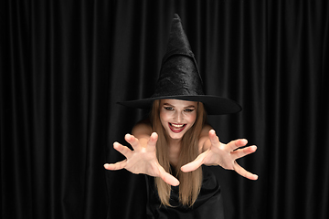 Image showing Young woman in hat as a witch on black background