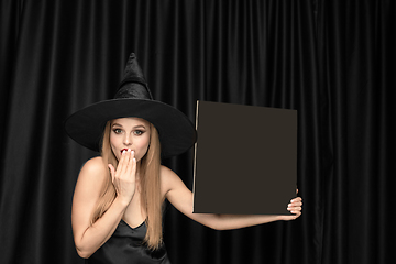 Image showing Young woman in hat as a witch on black background