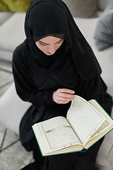 Image showing Portrait of young muslim woman reading Quran in modern home
