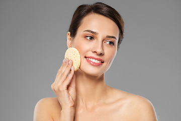 Image showing young woman cleaning face with exfoliating sponge