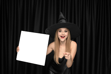 Image showing Young woman in hat as a witch on black background