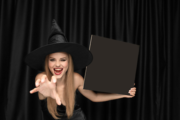 Image showing Young woman in hat as a witch on black background