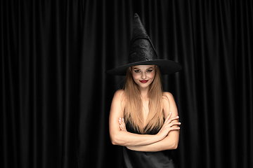 Image showing Young woman in hat as a witch on black background