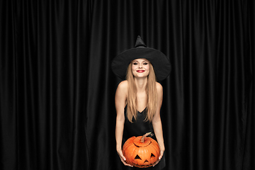 Image showing Young woman in hat as a witch on black background