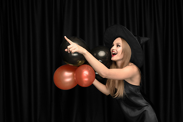 Image showing Young woman in hat as a witch on black background