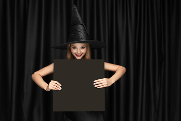 Image showing Young woman in hat as a witch on black background