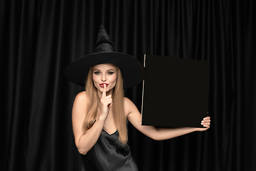 Image showing Young woman in hat as a witch on black background