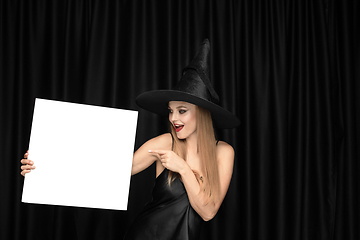 Image showing Young woman in hat as a witch on black background