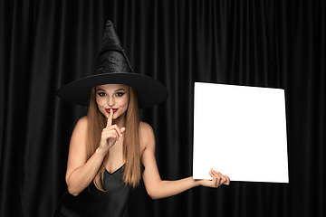 Image showing Young woman in hat as a witch on black background