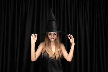 Image showing Young woman in hat as a witch on black background