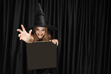 Image showing Young woman in hat as a witch on black background