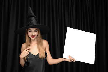 Image showing Young woman in hat as a witch on black background