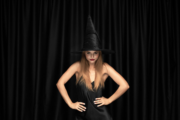 Image showing Young woman in hat as a witch on black background