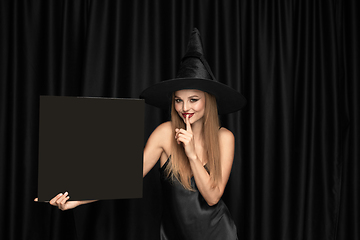 Image showing Young woman in hat as a witch on black background