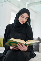 Image showing Portrait of young muslim woman reading Quran in modern home