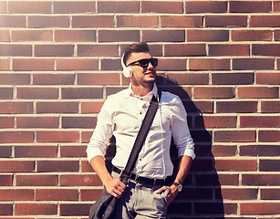 Image showing young man in headphones with bag over brickwall