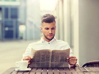 Image showing smiling man reading newspaper at city street cafe