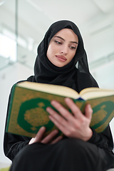 Image showing Portrait of young muslim woman reading Quran in modern home