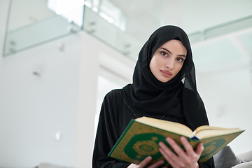 Image showing Portrait of young muslim woman reading Quran in modern home