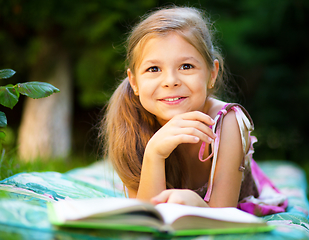 Image showing Little girl is reading a book outdoors