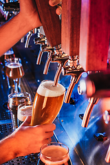 Image showing Hand of bartender pouring a large lager beer in tap