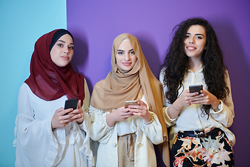 Image showing Muslim women using mobile phones isolated on blue and purple background