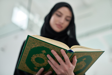 Image showing Portrait of young muslim woman reading Quran in modern home