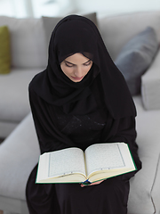 Image showing Portrait of young muslim woman reading Quran in modern home