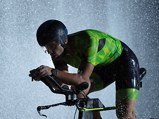 Image showing triathlon athlete riding bike on rainy night