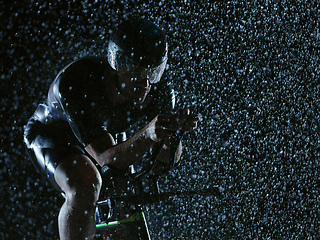 Image showing triathlon athlete riding bike on rainy night