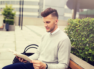 Image showing smiling man reading newspaper on city street bench