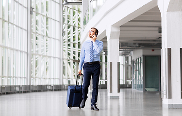 Image showing businessman with travel bag calling on smartphone