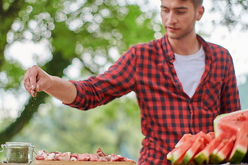 Image showing man putting spices on raw meat for barbecue