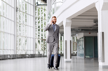 Image showing businessman with travel bag calling on smartphone