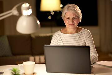 Image showing happy senior woman with laptop at home in evening