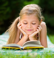 Image showing Little girl is reading a book outdoors